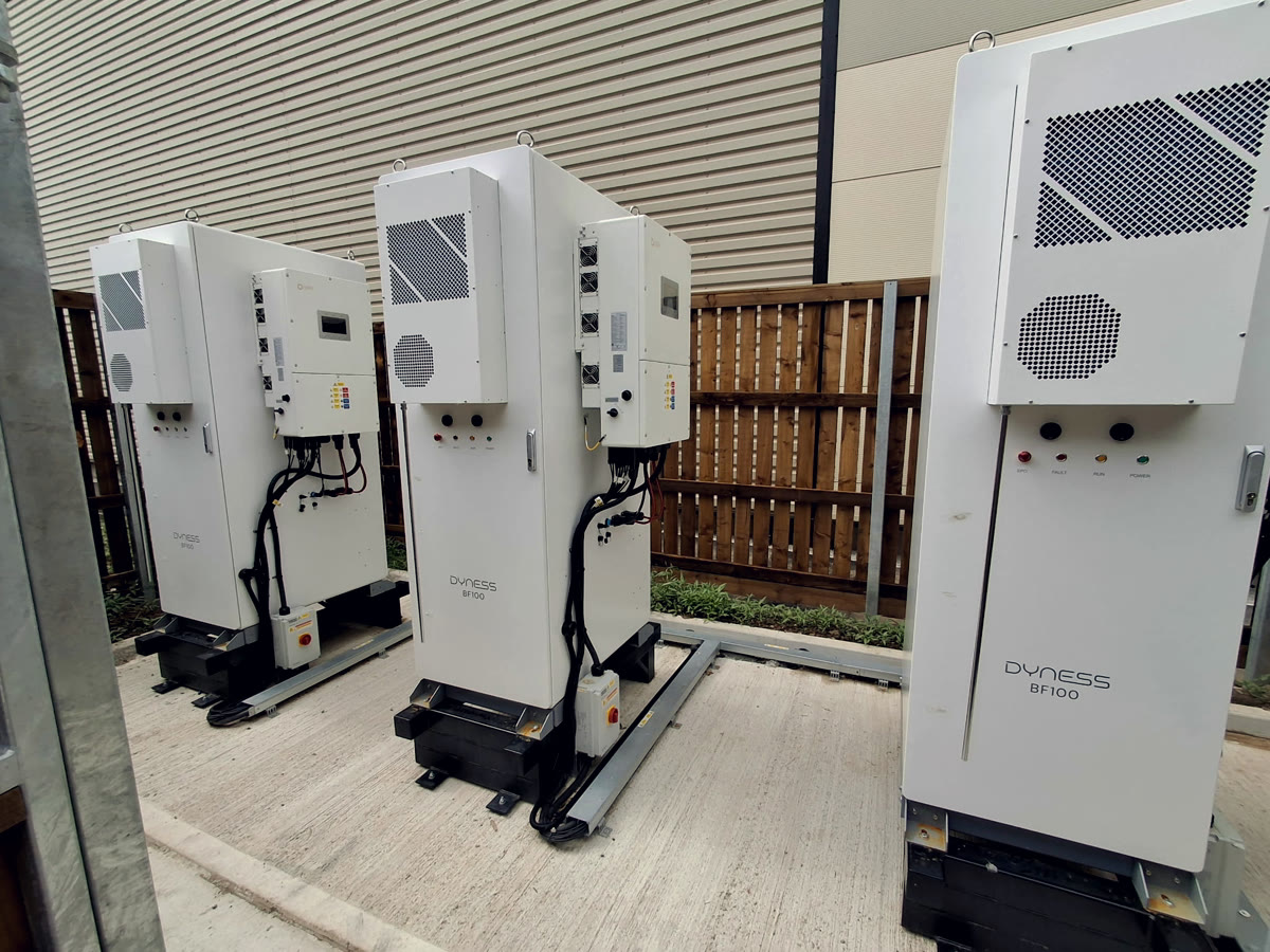 A row of Dyness BF100 battery cabinets with hybrid inverters, retrofitted by Novalux beside a commercial building